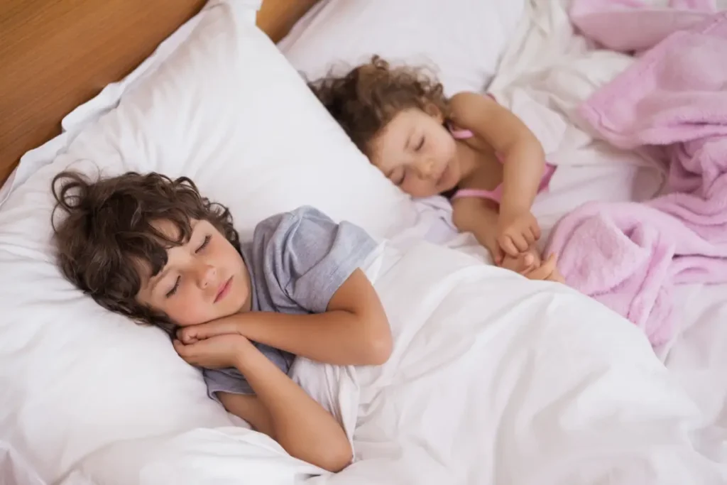 Two children sleeping comfortably in a cool, quiet bedroom at home